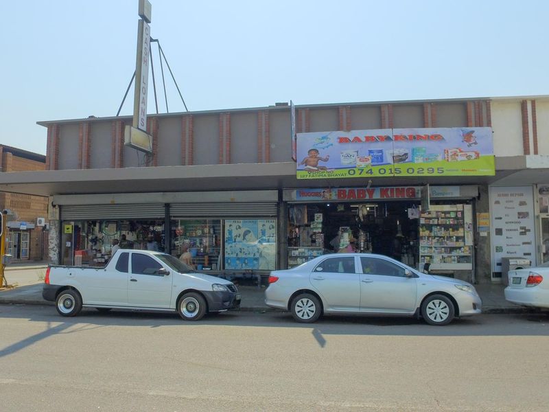 Street-level view of a commercial retail shopfront featuring roller shutter doors, signage, and a covered walkway in a busy urban business district.