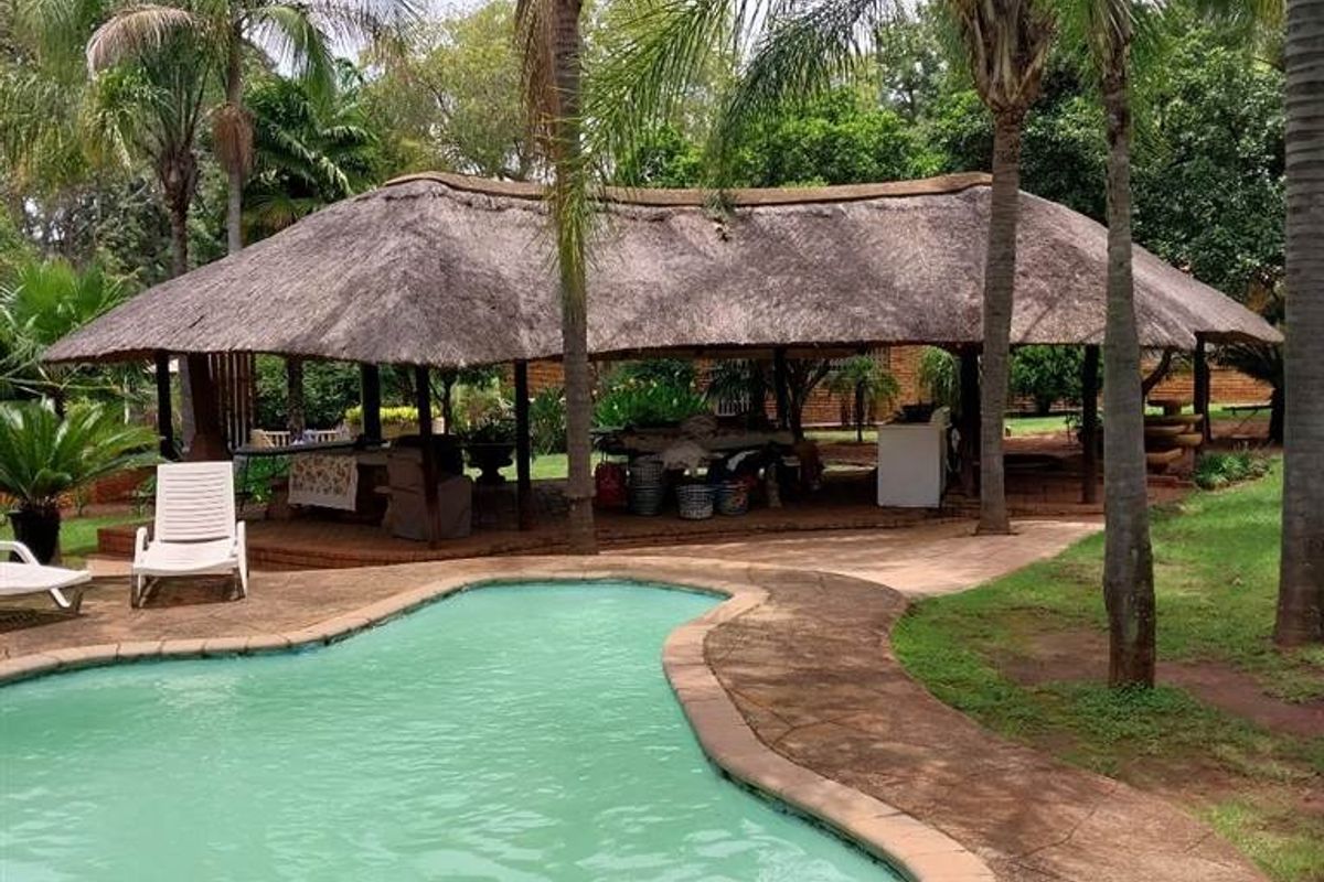 Outdoor pool area featuring a large swimming pool with stone coping and a spacious thatched lapa for entertainment.