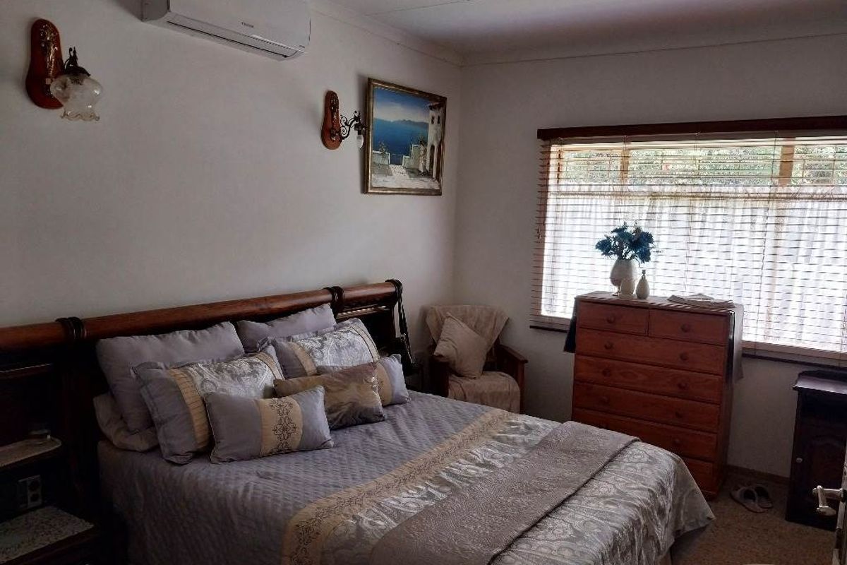 A comfortable bedroom featuring a wall-mounted split-system air conditioner, venetian blinds, and classic wall lighting fixtures.