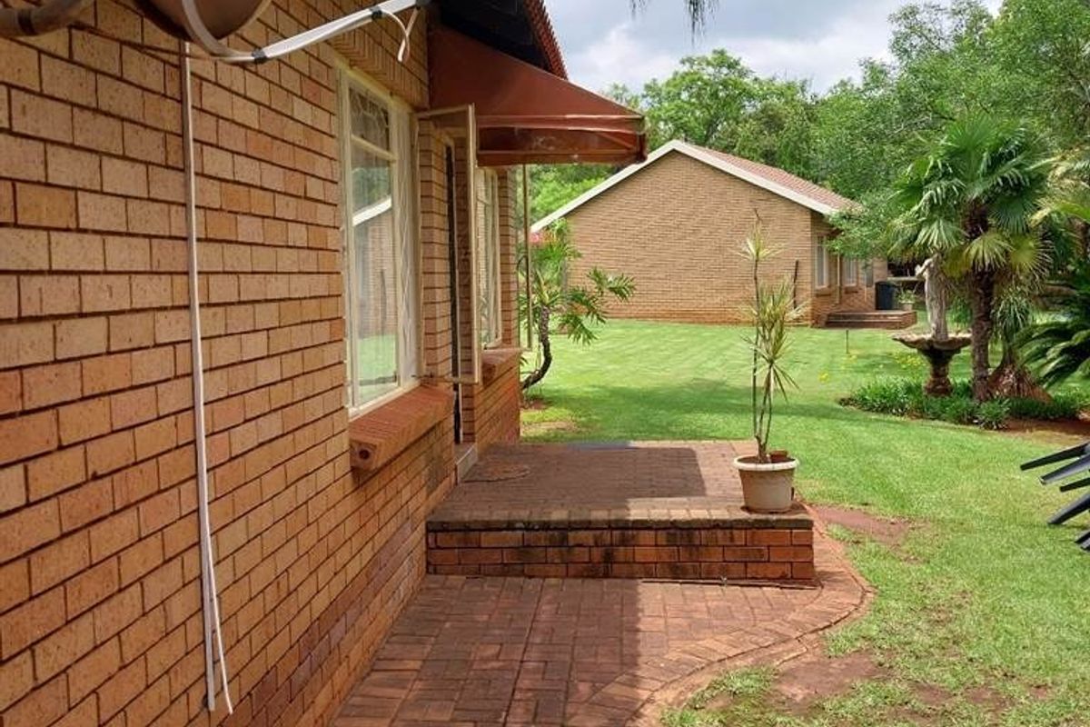 Rear view of a brick farmhouse featuring a paved walkway, brick steps, and a well-maintained lawn area with mature trees.