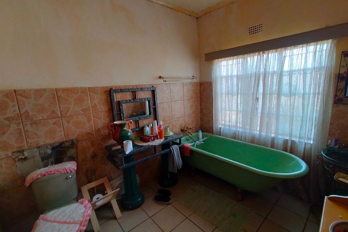 A dated bathroom featuring a vintage green freestanding bathtub, pedestal basin, and ceramic tiling, requiring significant renovation and cosmetic updates.