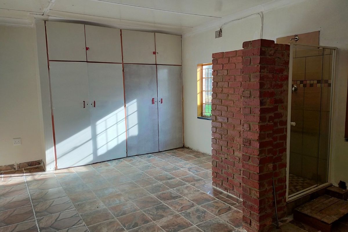 A bedroom featuring built-in cupboards, an exposed brick partition wall, and an integrated shower enclosure with tiled flooring throughout.