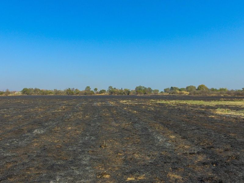 An aerial view of a large, flat, vacant commercial land plot showing signs of recent vegetation clearing or fire damage.