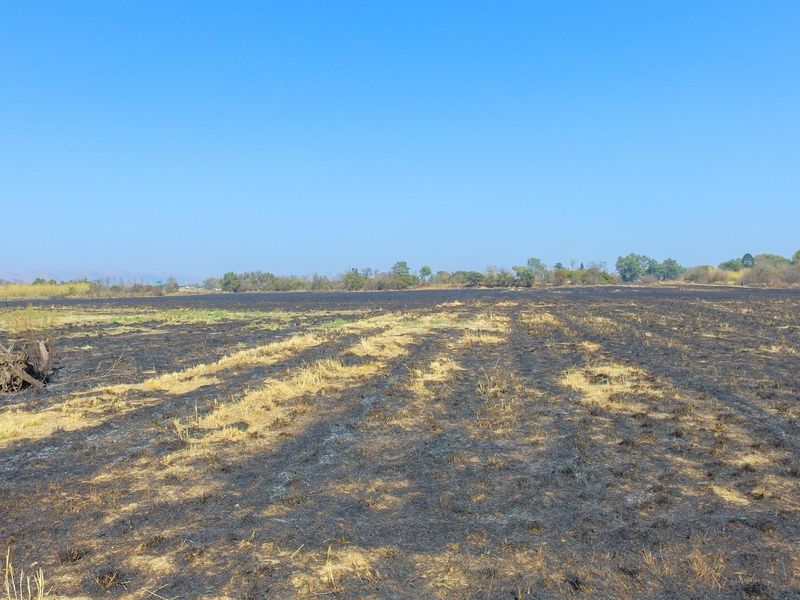 A wide view of a vacant commercial land plot showing signs of recent vegetation burning across the field.
