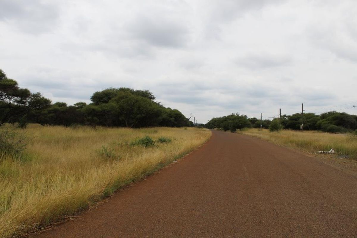 A view of a paved road running alongside a vacant commercial land plot with natural vegetation and utility infrastructure.