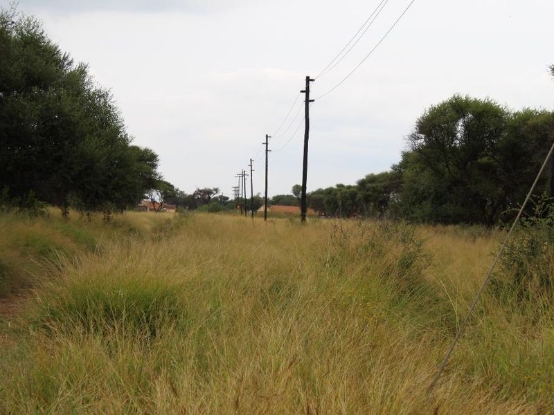 A view of a vacant commercial land plot featuring natural grassland and existing overhead utility infrastructure.
