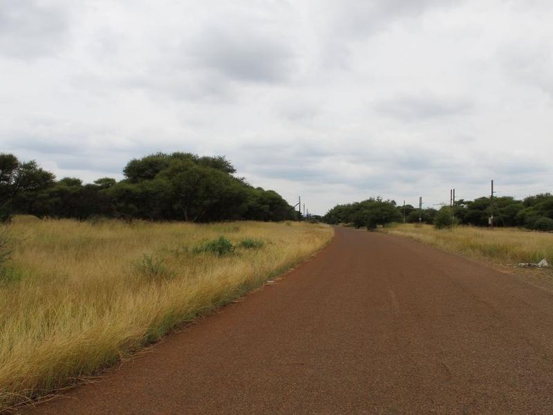 A view of a paved road running alongside a vacant commercial land plot with natural vegetation and utility infrastructure.