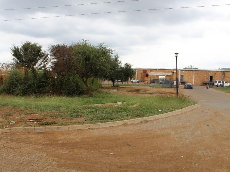 A view of the vacant commercial land featuring a paved driveway, perimeter fencing, and established trees, providing access to the adjacent industrial building.
