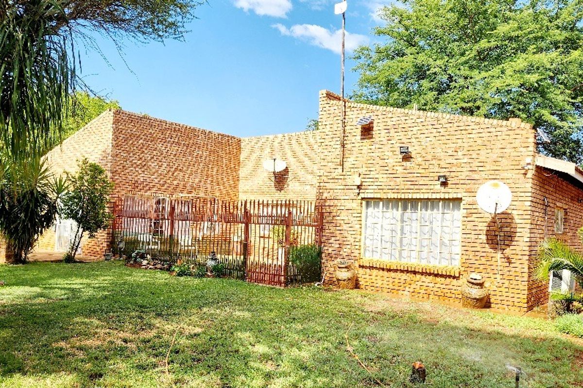 Rear view of a face brick farm property featuring a lawn, security fencing, and exterior wall lighting.