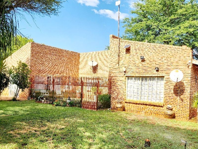 Rear view of a face brick farm property featuring a lawn, security fencing, and exterior wall lighting.