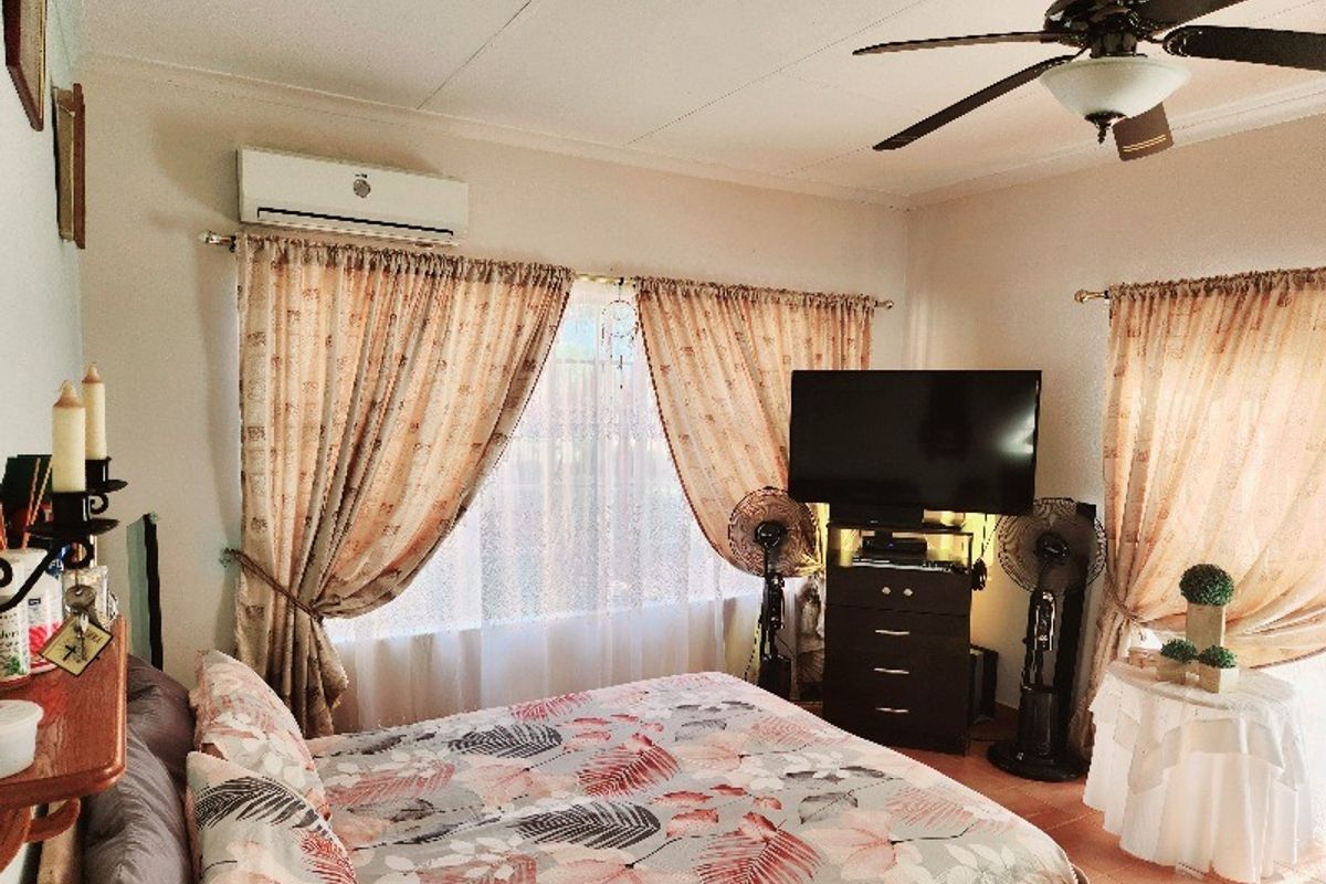 A bedroom featuring a ceiling fan, split-system air conditioning unit, and tiled flooring, offering a functional space with natural light.