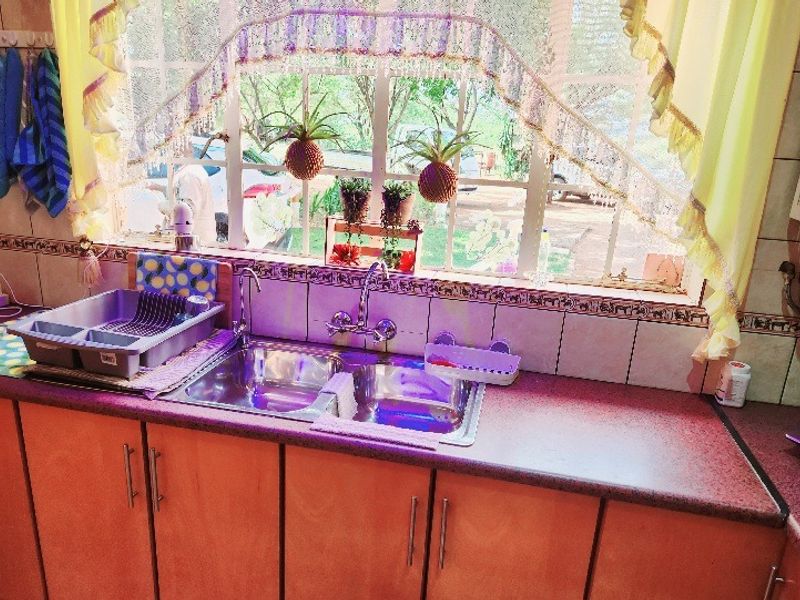 A functional kitchen area featuring a double stainless steel sink, tiled backsplash, and ample built-in cabinetry with laminate countertops.