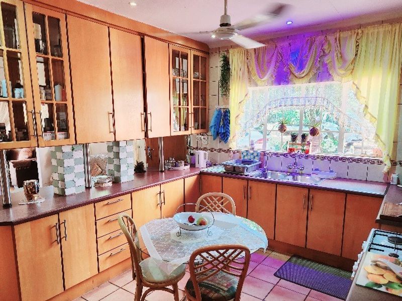 A functional kitchen featuring extensive wooden cabinetry, laminate countertops, a double basin sink, and a gas hob, with a bright window overlooking the garden.