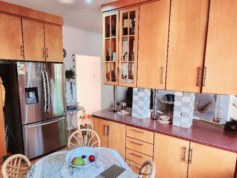 A functional kitchen featuring warm-toned wooden cabinetry, laminate countertops, and a built-in stainless steel refrigerator, offering ample storage and prep space.