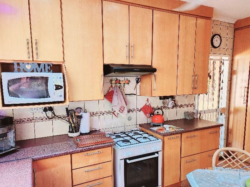 A functional kitchen featuring light wood cabinetry, a gas stove with an extractor fan, and tiled backsplash, offering a traditional farm-style aesthetic.