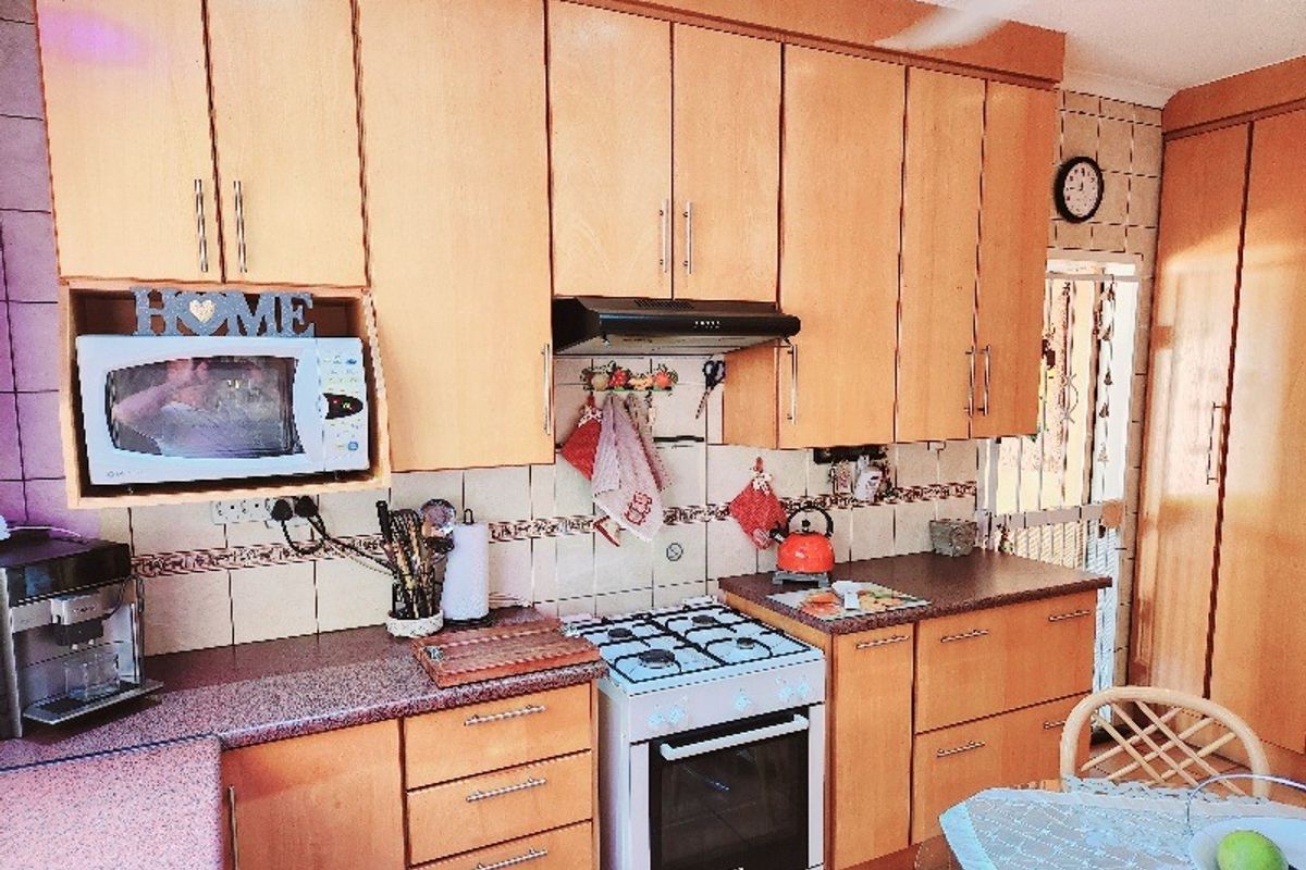 A functional kitchen featuring light wood cabinetry, a gas stove with an extractor fan, and tiled backsplash, offering a traditional farm-style aesthetic.