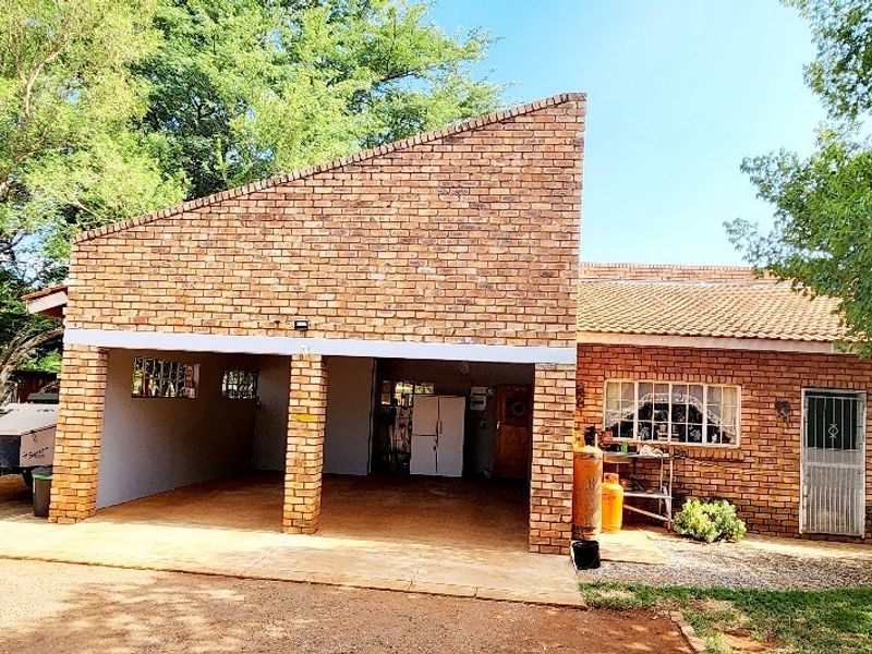 Front view of a brick farmhouse featuring a covered carport area, tiled roofing, and secure entrance with security gate.