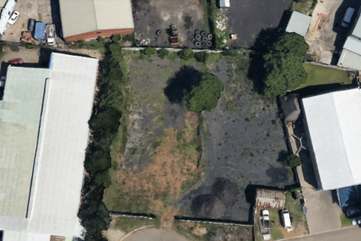 Aerial view of a vacant commercial land parcel featuring boundary fencing and mature trees, situated between existing industrial structures.