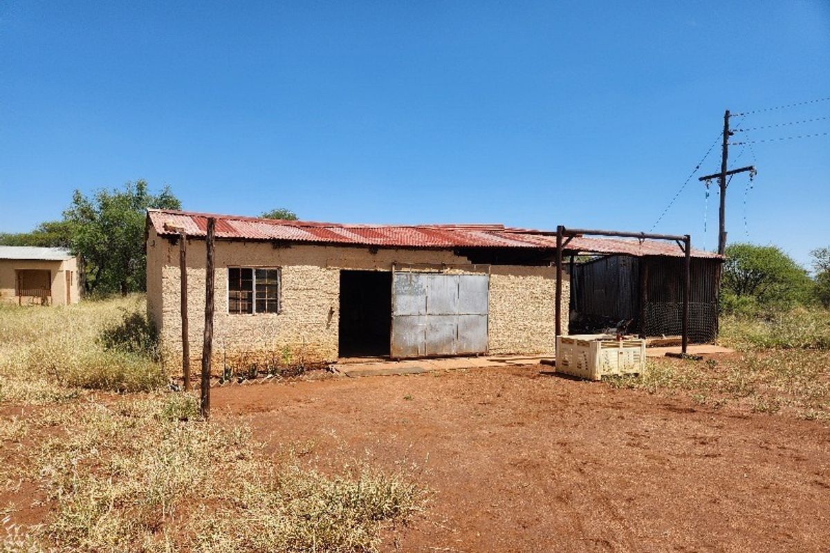 A view of a basic commercial structure on vacant land featuring a corrugated metal roof and metal sliding door access.
