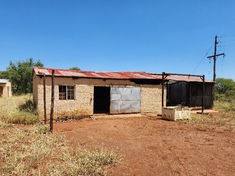 A view of a basic commercial structure on vacant land featuring a corrugated metal roof and metal sliding door access.