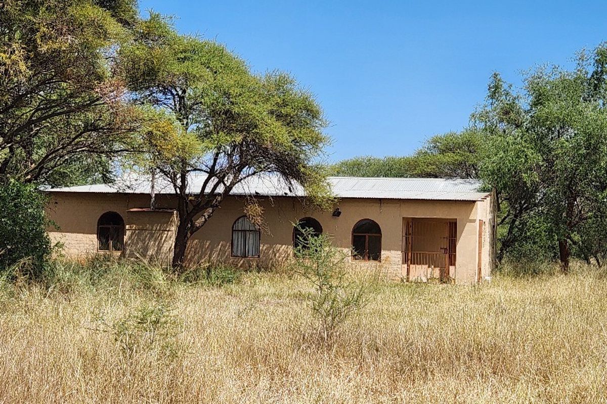 A single-story commercial building structure featuring arched windows and a covered entrance, situated on a large, undeveloped plot of land.