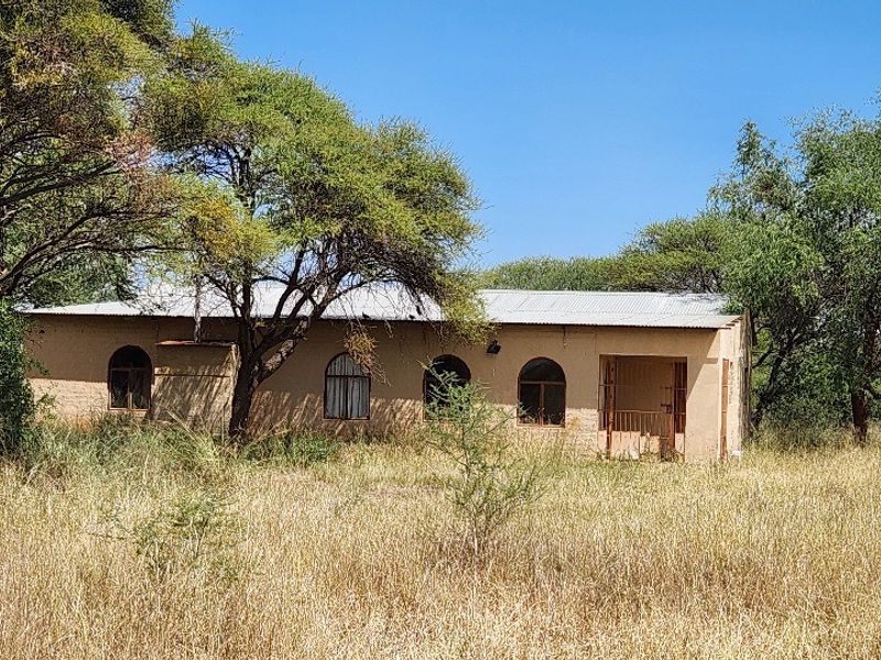 A single-story commercial building structure featuring arched windows and a covered entrance, situated on a large, undeveloped plot of land.