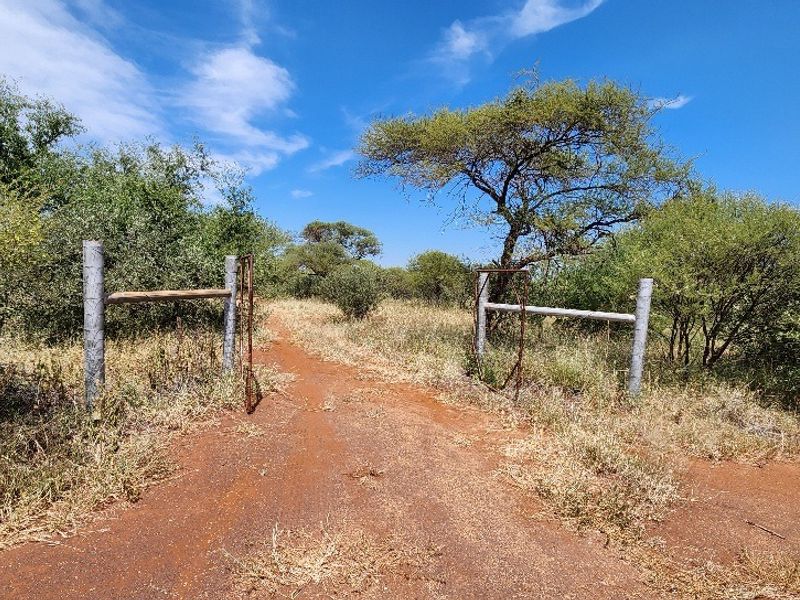 A view of the property entrance featuring a dirt access road and basic metal gate infrastructure surrounded by natural bushveld vegetation.