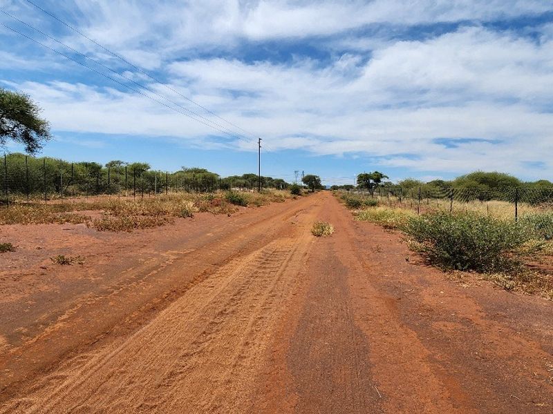 A view of a dirt access road leading through the vacant commercial land, featuring perimeter wire fencing and overhead utility lines.