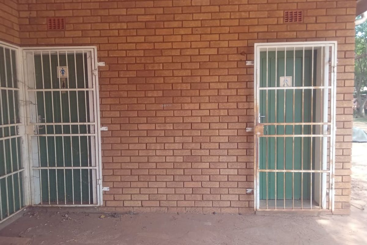 Exterior view of a commercial building featuring exposed brick walls, security gates, and ventilation bricks, with a concrete apron area.