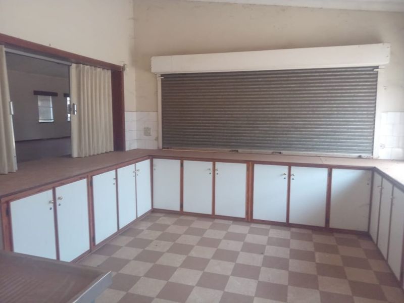 A functional commercial kitchen area featuring extensive built-in cabinetry, a secure roller shutter service window, and durable tiled flooring.