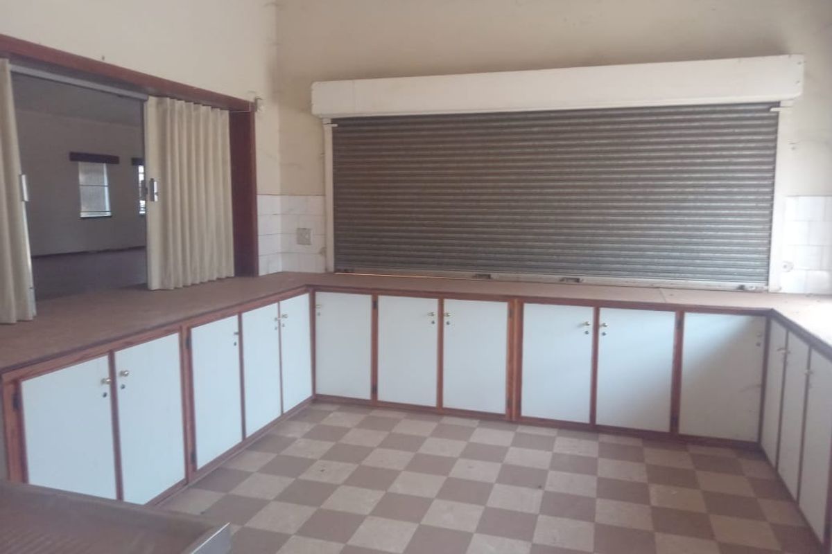 A functional commercial kitchen area featuring extensive built-in cabinetry, a secure roller shutter service window, and durable tiled flooring.