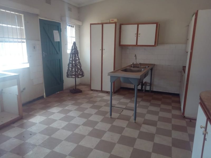 A functional scullery or utility area featuring a stainless steel double sink, built-in cabinetry, and checkered flooring, offering potential for modernization.