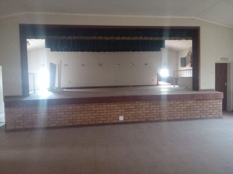 A large commercial hall featuring a raised stage with brick detailing and integrated curtains, suitable for events or community gatherings.