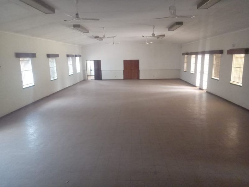 A large, open-plan commercial space featuring tiled flooring, multiple ceiling fans, and abundant natural light through numerous windows with venetian blinds.
