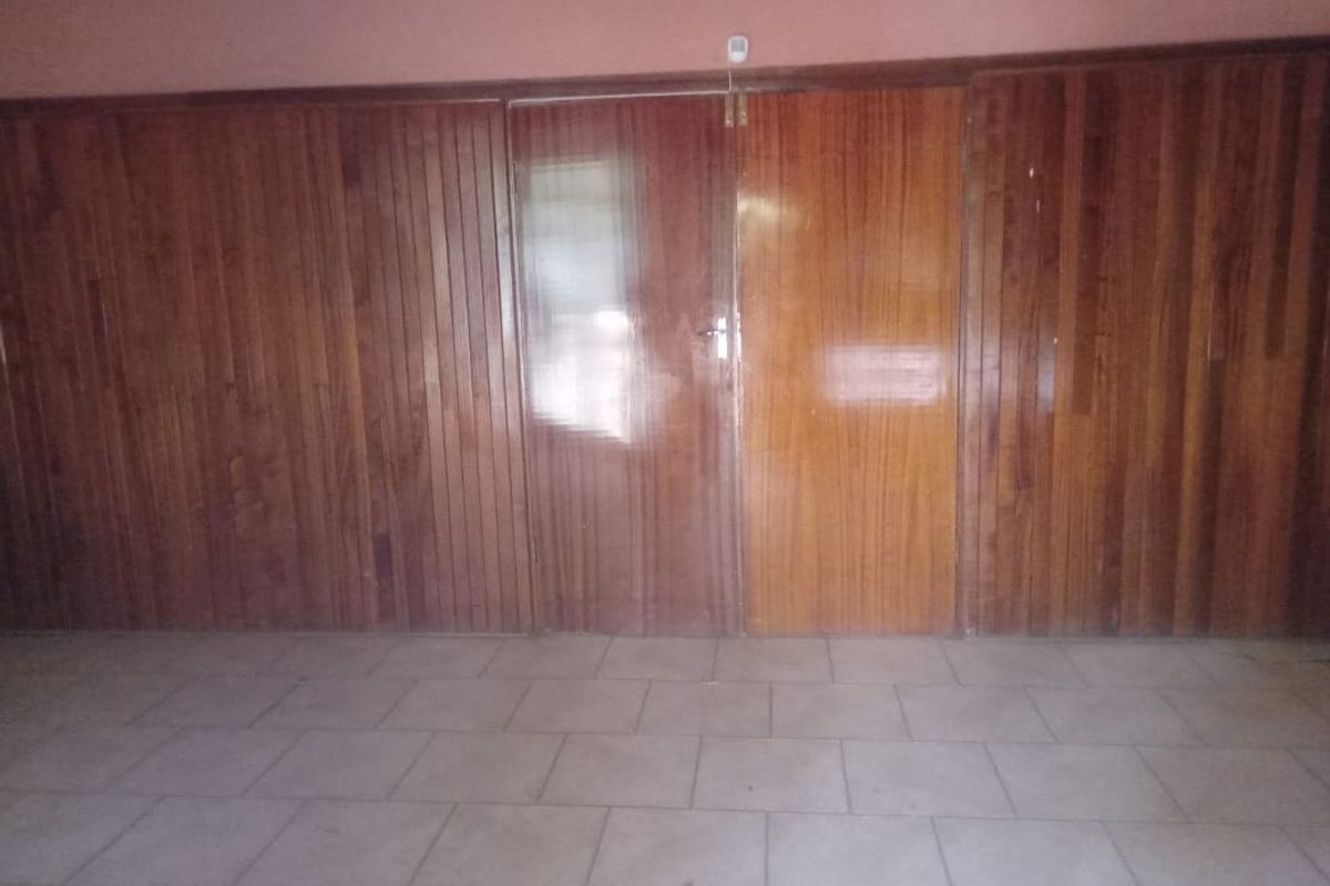 An empty room featuring extensive timber wall paneling, double timber doors, and ceramic tiled flooring, offering a dated aesthetic ready for modernization.