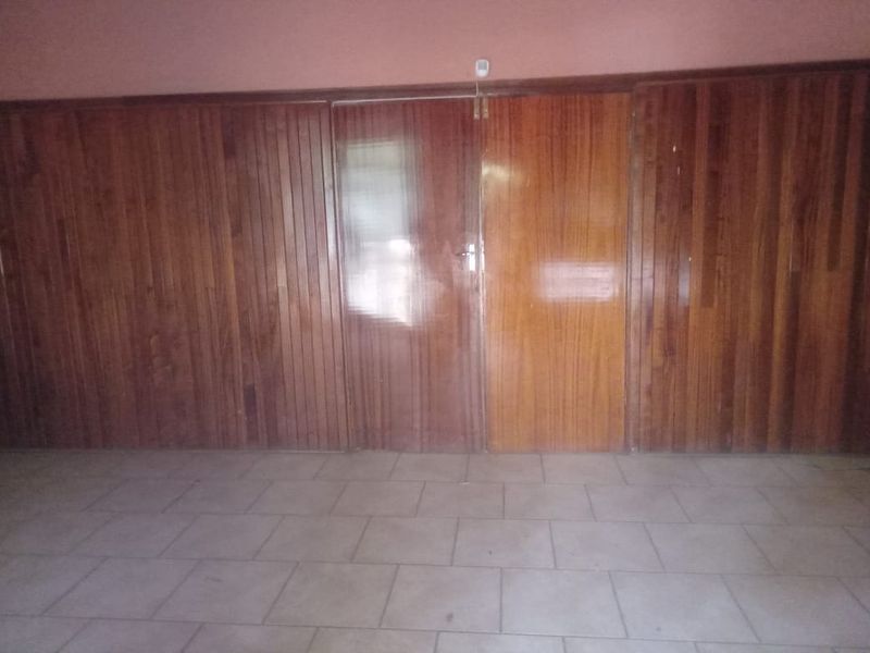 An empty room featuring extensive timber wall paneling, double timber doors, and ceramic tiled flooring, offering a dated aesthetic ready for modernization.