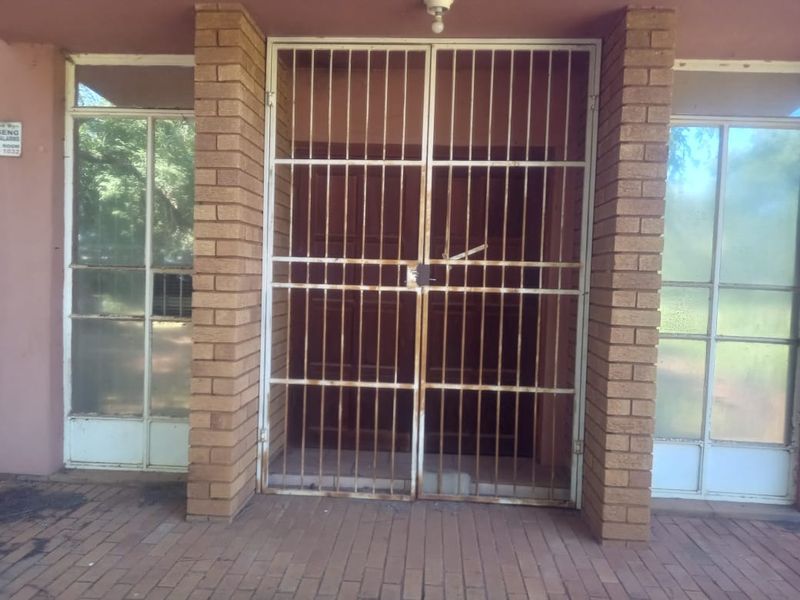 Commercial building entrance featuring a paved walkway, brick pillars, and a secure metal gate with adjacent glass panel windows.