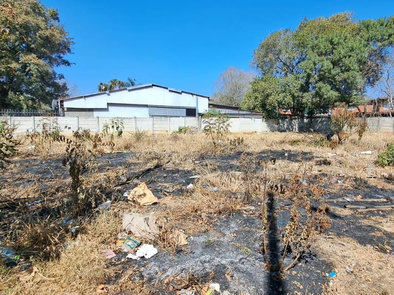 A vacant commercial land plot featuring a precast concrete boundary wall, currently showing signs of overgrown vegetation and surface debris.