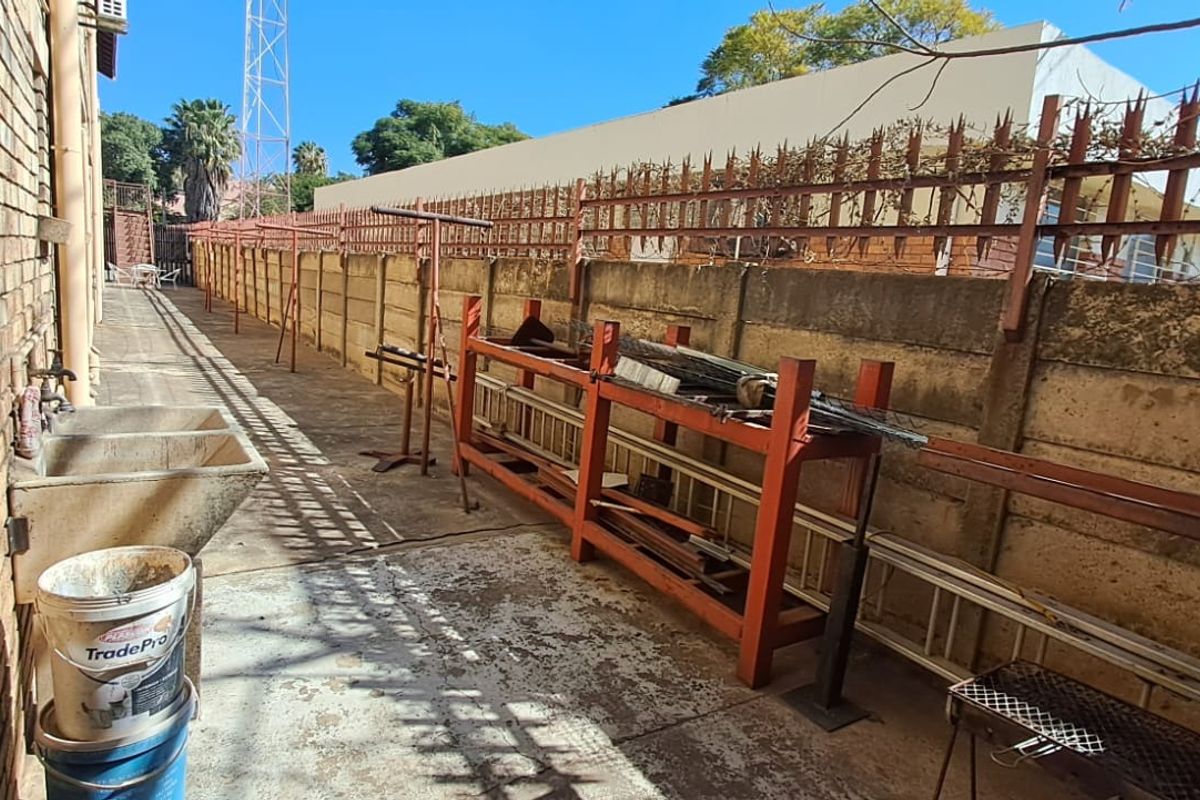 A narrow rear exterior service area featuring a concrete boundary wall with security spikes, paved flooring, and a fixed utility sink.