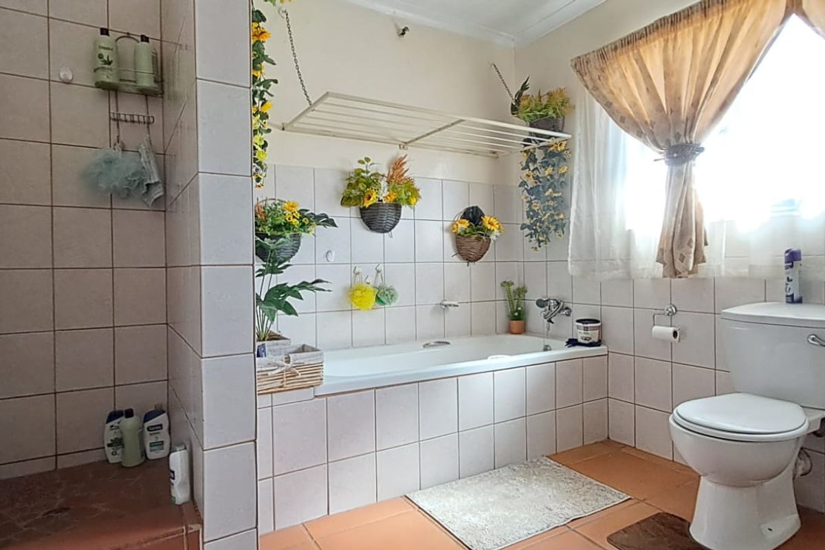 A functional bathroom featuring a built-in bathtub, tiled walls and flooring, and a standard toilet suite with natural light from the window.