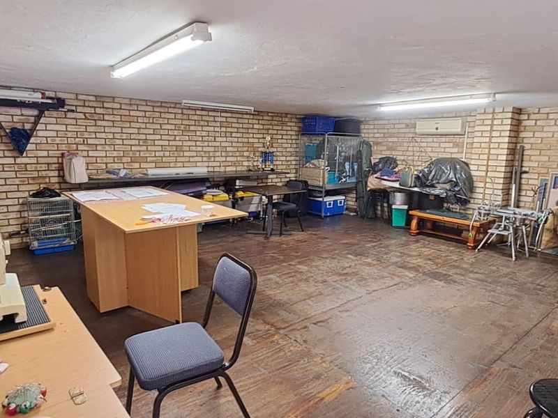 A spacious utility room featuring exposed brick walls, timber flooring, and functional strip lighting, suitable for storage or a workshop area.