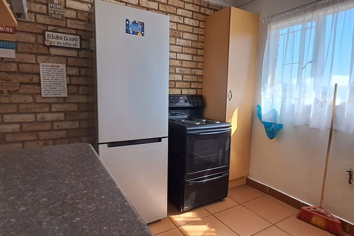 A functional kitchen featuring exposed brick walls, tiled flooring, built-in cabinetry, and a freestanding stove, offering a practical layout for daily use.