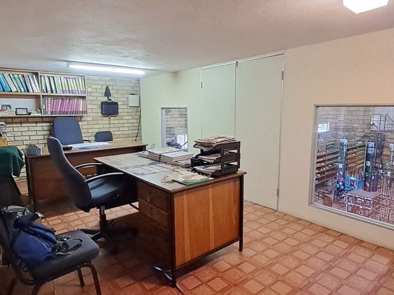 Functional office space featuring exposed brick walls, built-in shelving, and an internal window overlooking the retail area.