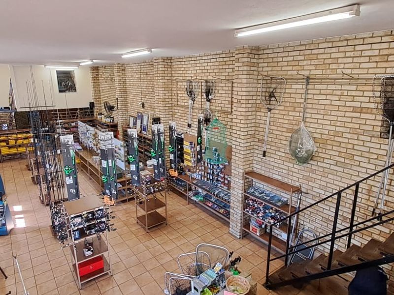 Spacious retail interior featuring exposed brick walls, tiled flooring, and a mezzanine level accessed by a metal staircase, currently utilized as a fishing supply store.