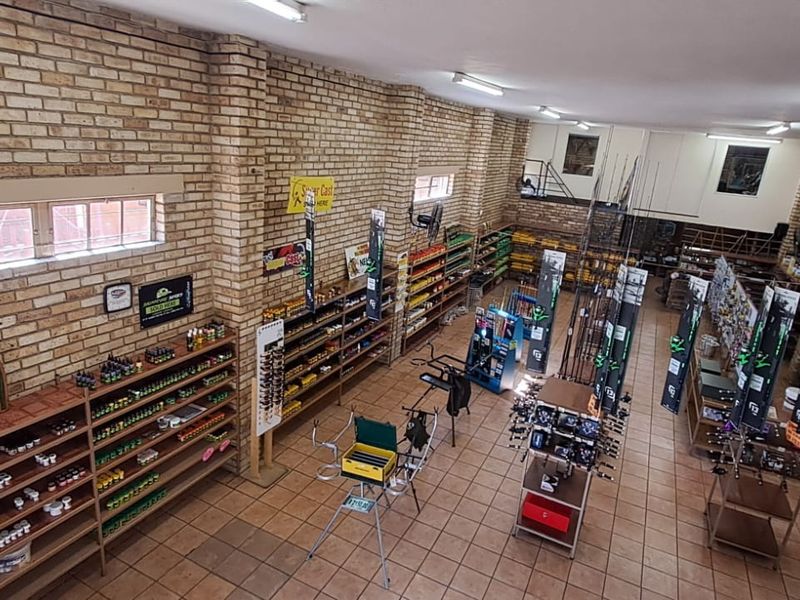 Spacious retail interior featuring exposed brick walls, tiled flooring, and extensive built-in shelving, currently utilized as a fishing supply store.