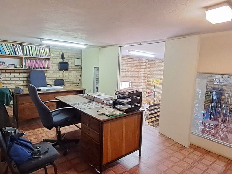 A functional office space featuring exposed brick walls, built-in shelving, and an internal window overlooking the retail area.