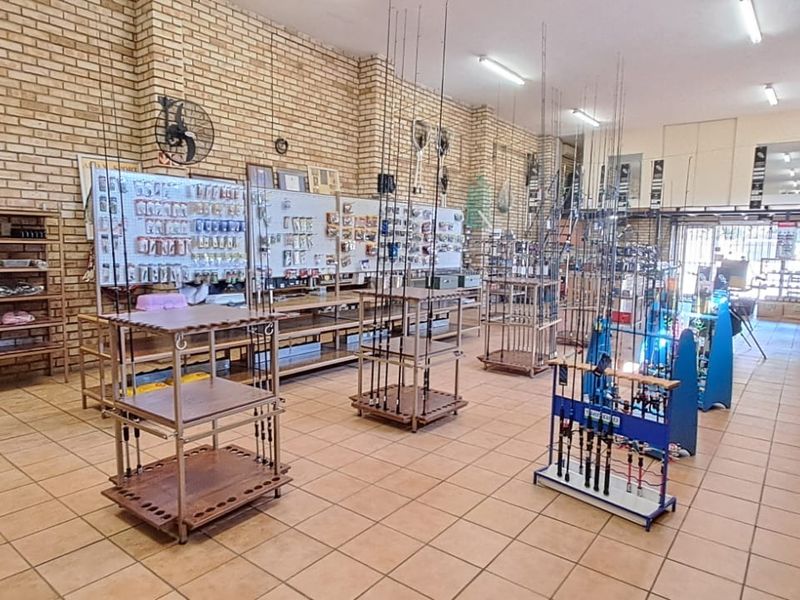 Spacious retail interior featuring exposed brick walls, durable ceramic tile flooring, and functional overhead fluorescent lighting, currently configured for a fishing supply store.