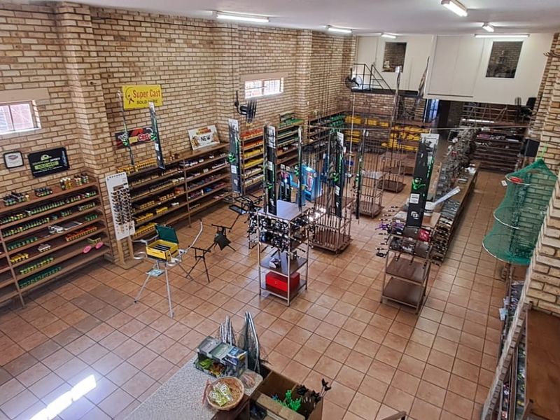 Spacious retail interior featuring exposed brick walls, tiled flooring, built-in shelving units, and a mezzanine level, currently utilized as a fishing supply store.