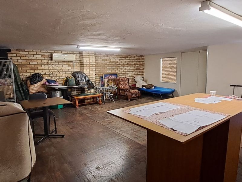 A functional utility space featuring exposed brick walls, fluorescent lighting, and a split-system air conditioner, suitable for storage or workshop use.