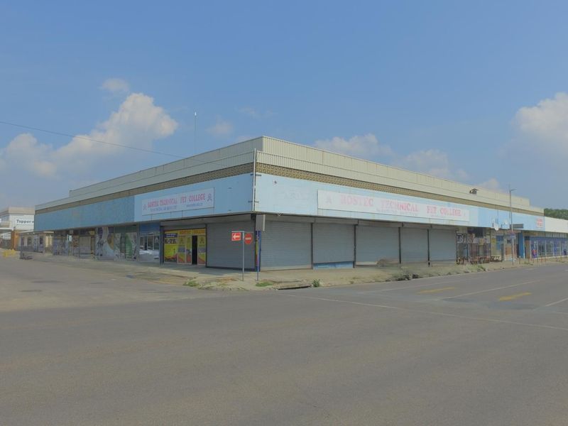 Corner retail building featuring large glass storefronts and secure metal roller shutters, situated at a prominent street intersection.